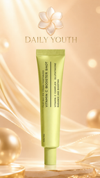 A light yellow-green squeeze tube of Daily Youth Vitamin C Booster Shot face and eye cream moisturizer, set against a warm golden background with elegant ribbons and soft bokeh lights.